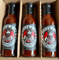 Three bottles of Miller & Son BBQ Sauce Brewing Co. hot sauce arranged in a cardboard tray.