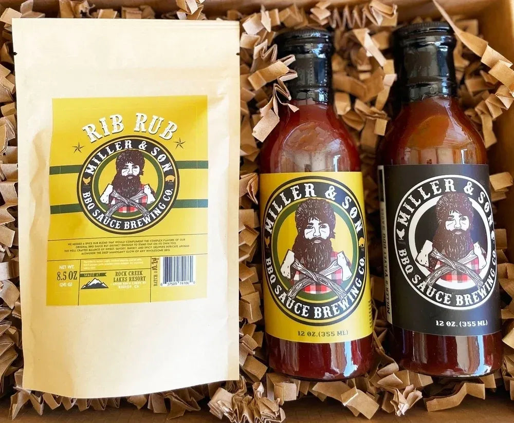 Miller & Son BBQ Sauce Brewing Co. gift set in a box with crinkle paper filler, featuring a white pouch and two bottles of sauce with black and yellow labels.